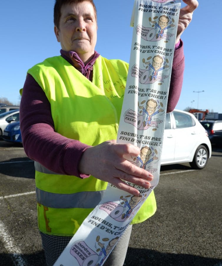 Une Gilet Jaune tient du papier toilette à l’effigie de Macron